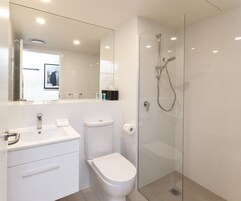 Un baño moderno con ducha de vidrio, lavamanos blanco y retrete.