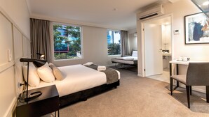 A modern hotel room with a large bed, bedside table, lamp, and a view of the city through large windows. - Woodroffe Hotel (Southport)