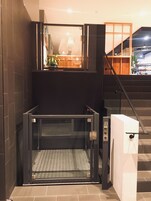 Un ascenseur moderne doté d’une porte en verre, d’une rampe métallique et d’un panneau de commande.