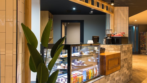 A modern interior with a central counter displaying food items, a potted plant, and a brick wall design. - Woodroffe Hotel (Southport)