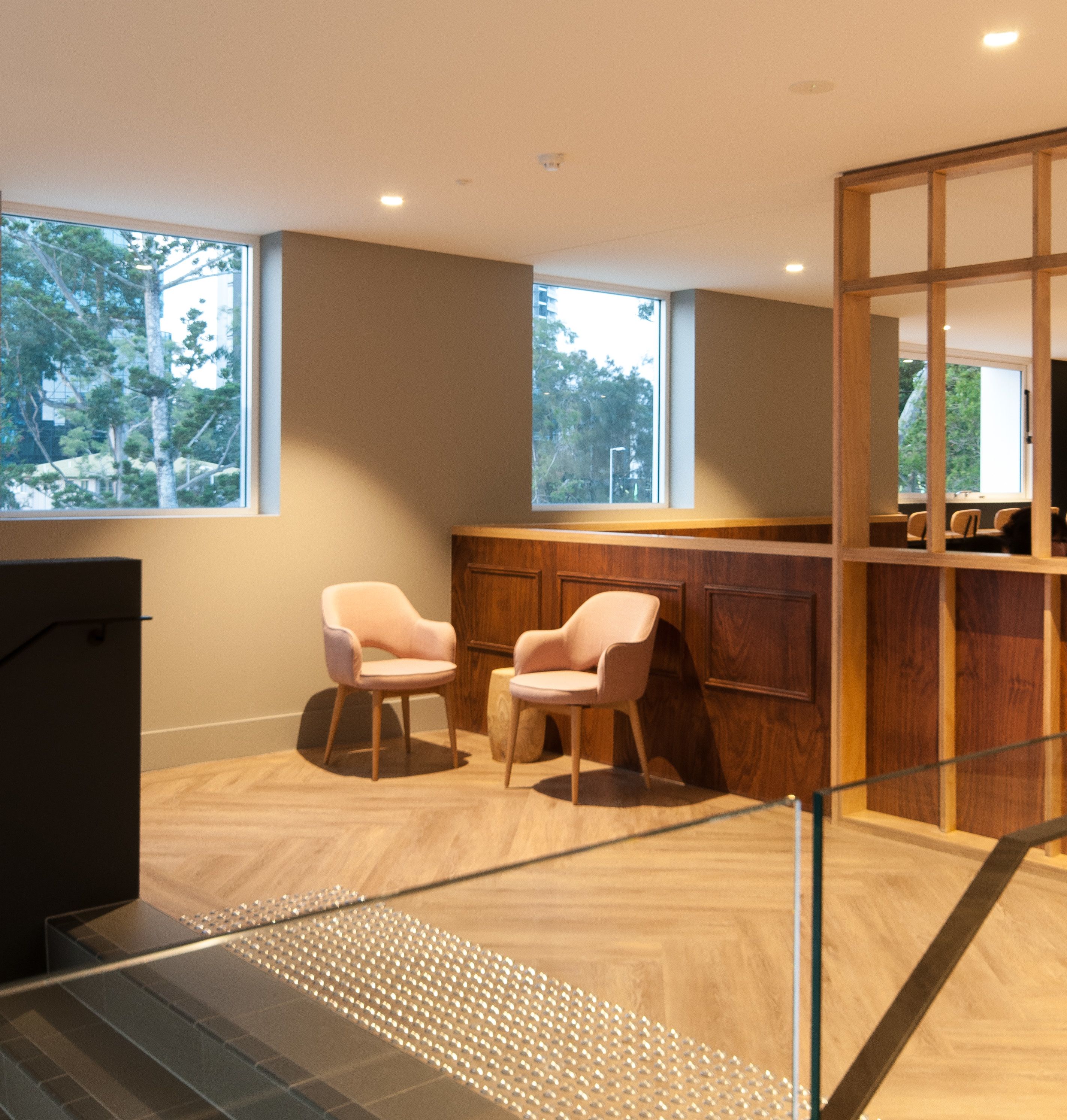 A modern interior with two pink chairs, a wooden counter, and large windows.