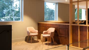 A modern interior with two pink chairs, a wooden counter, and large windows.