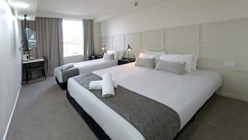Une chambre d’hôtel avec deux lits, un bureau, une chaise, une télévision et une fenêtre avec des rideaux.