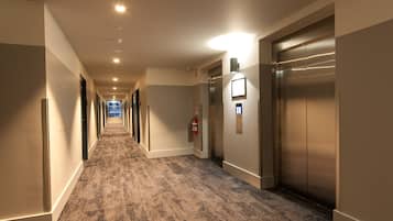 Un couloir d'hôtel avec des revêtements de sol en moquette, un extincteur et un ascenseur.