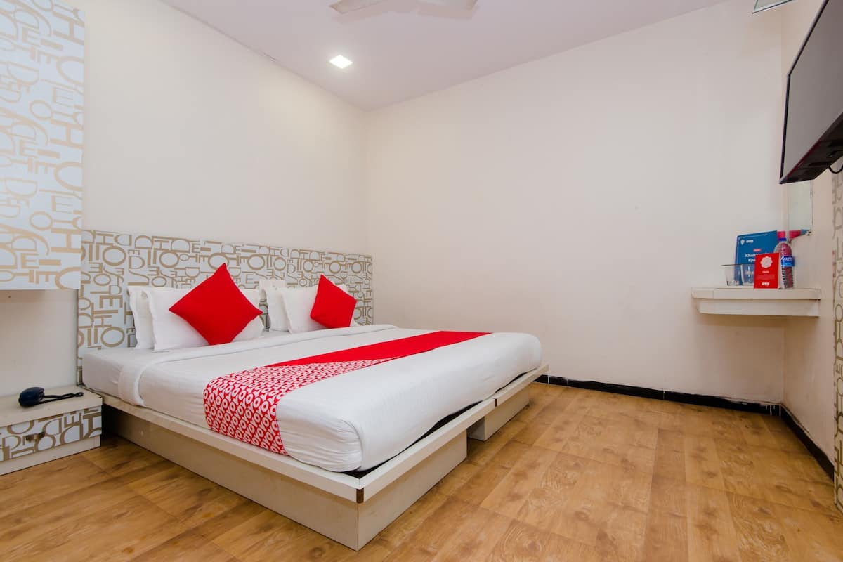 Ein ordentlich bezogenes Bett mit weißer Bettwäsche und roten Akzenten, ein Nachttisch mit Telefon sowie ein an der Wand befestigtes Regal mit Gegenständen.