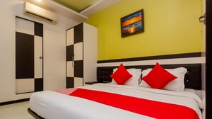 A hotel room with a bed, a nightstand, a red and white bedspread, a painting on the wall, and a checkered closet. - OYO 3769 Blue Pearl Residency (Mumbai)