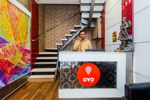 Un comptoir d’accueil d’hôtel agrémenté d’un tableau abstrait aux couleurs vives, d’un escalier et d’une statue.