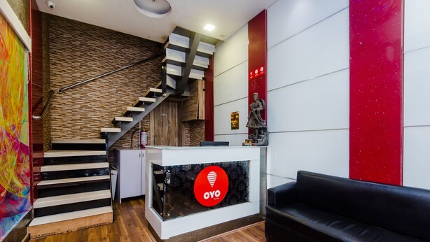 A reception area with a staircase, a reception desk with a logo, a statue, and a black leather sofa. - OYO 3769 Blue Pearl Residency (Mumbai)