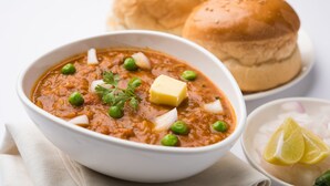 A bowl of curry with peas and a cube of butter, accompanied by a bun and a lemon wedge. - OYO 3769 Blue Pearl Residency (Mumbai)