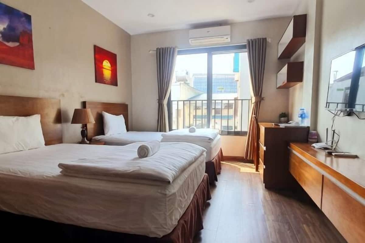 Habitación de hotel con dos camas, un escritorio, una silla, un televisor y una ventana con cortinas.