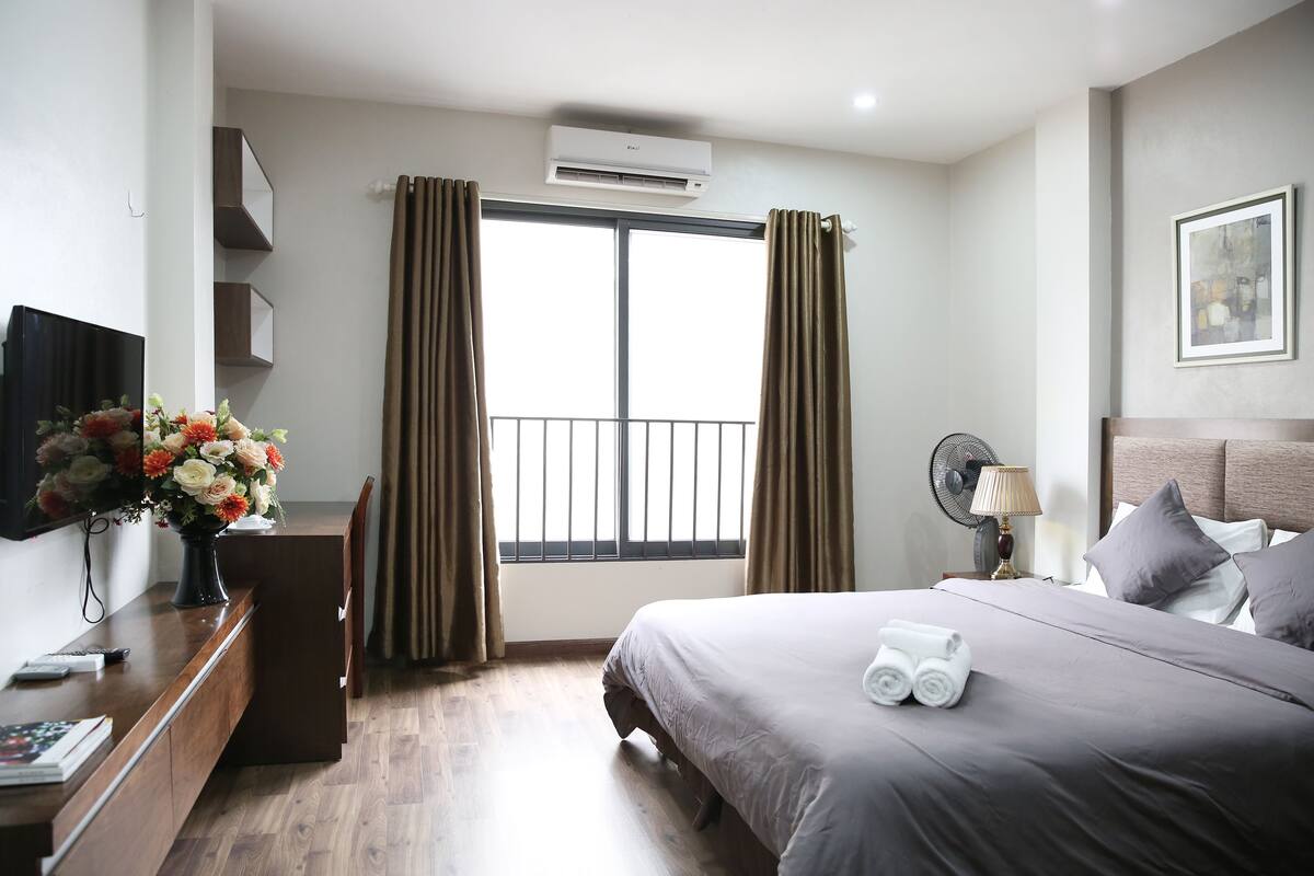 Habitación de hotel con cama, mesita de noche, televisión y ventana con cortinas.