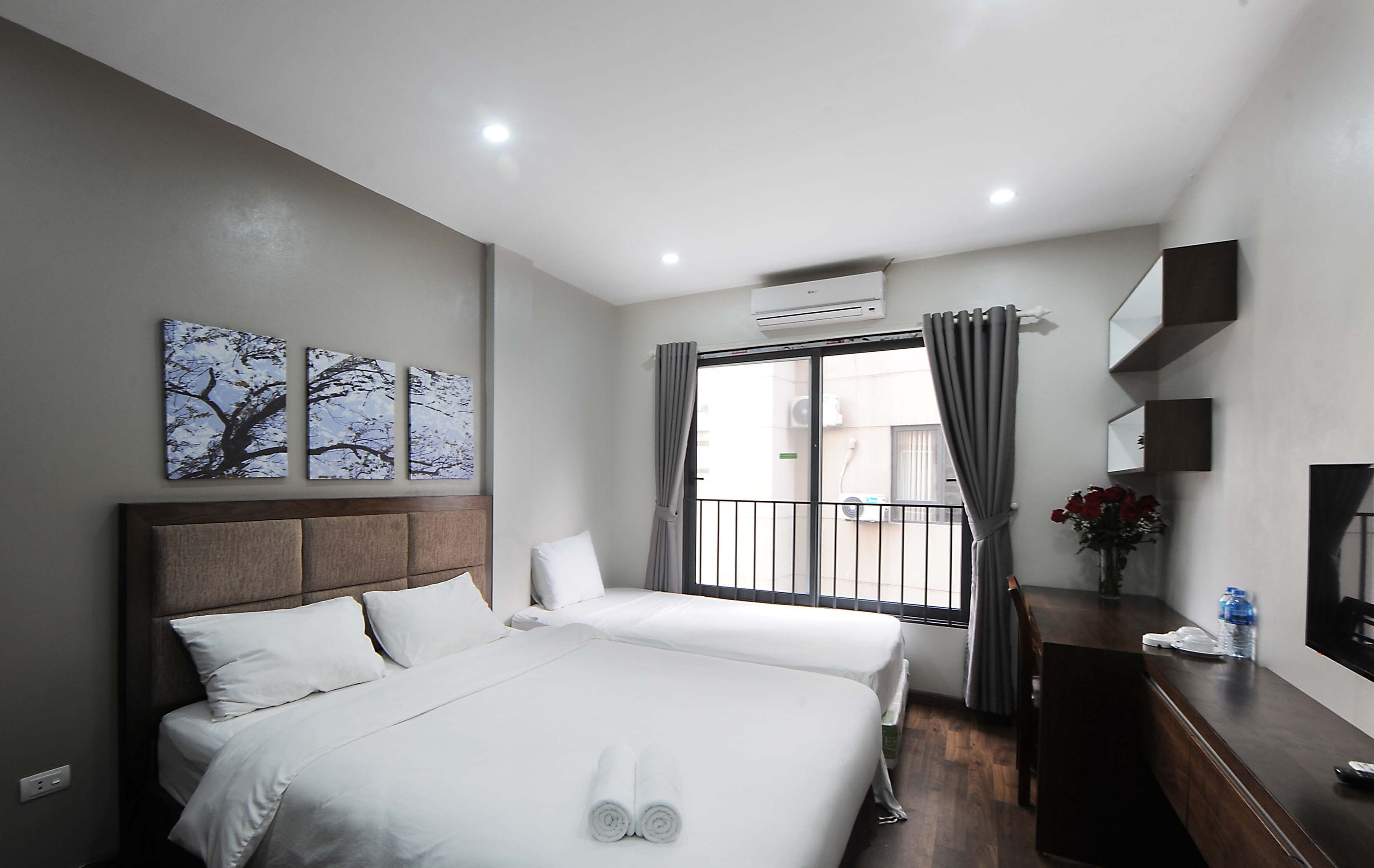 A hotel room with two beds, a large window with curtains, an air conditioning unit, a wooden dresser, and artwork on the wall.