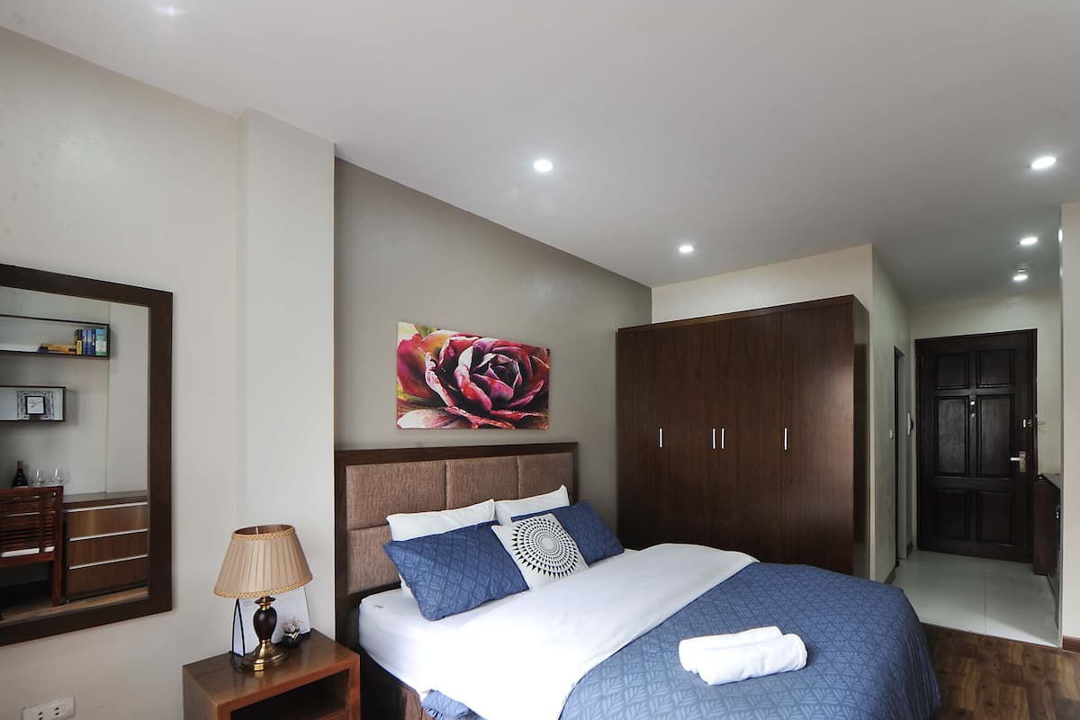 Un dormitorio ordenado con cama, mesita de noche, espejo, armario y puerta.