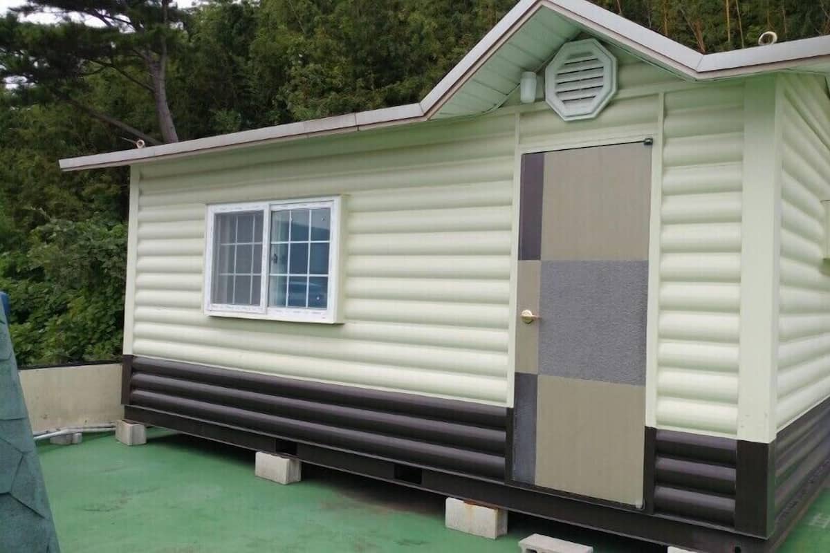 A small, single-story mobile home with a window, a door, and a small porch area.