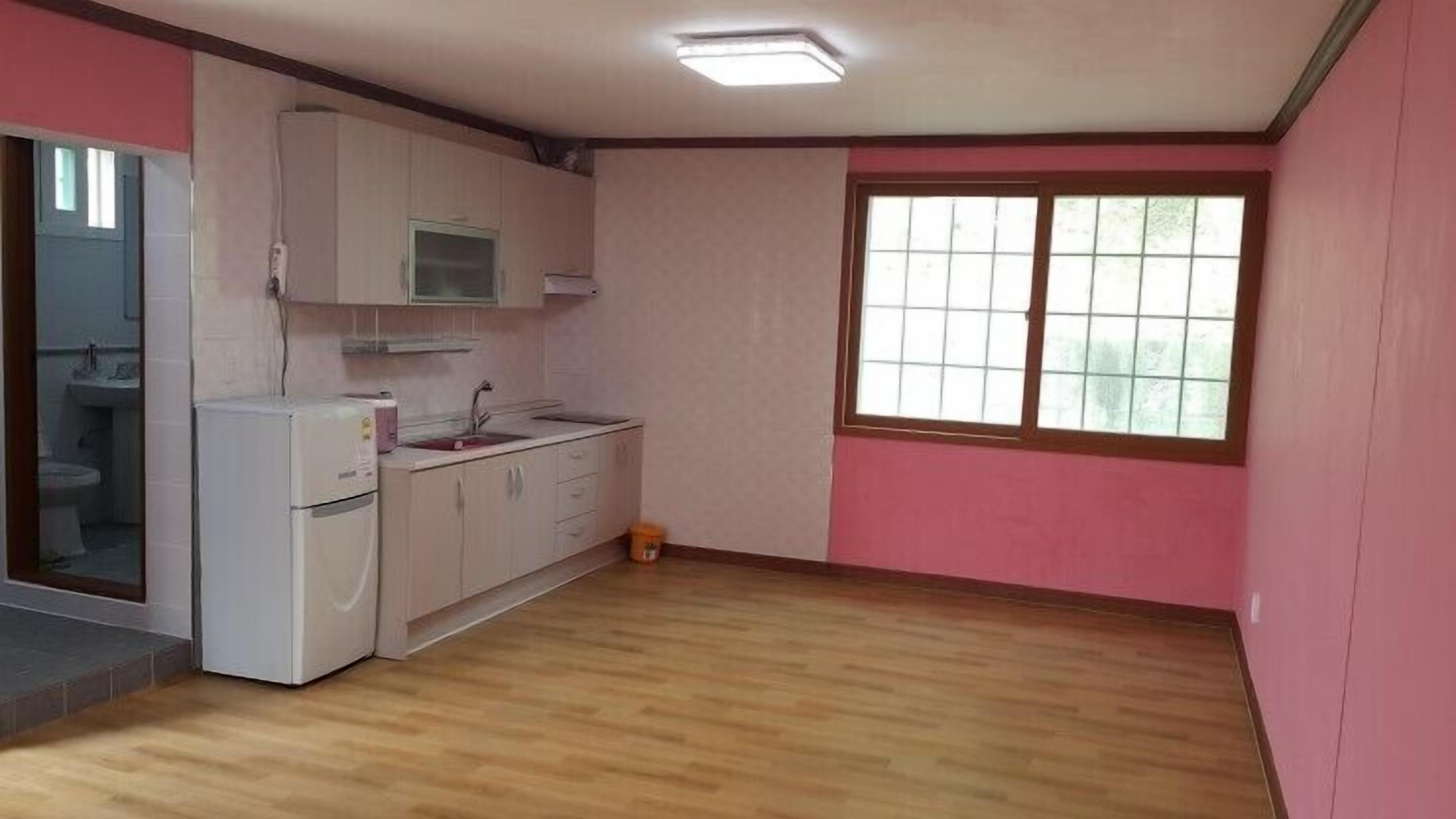A small kitchen with a microwave, sink, and cabinets. There is a window with a view of trees.