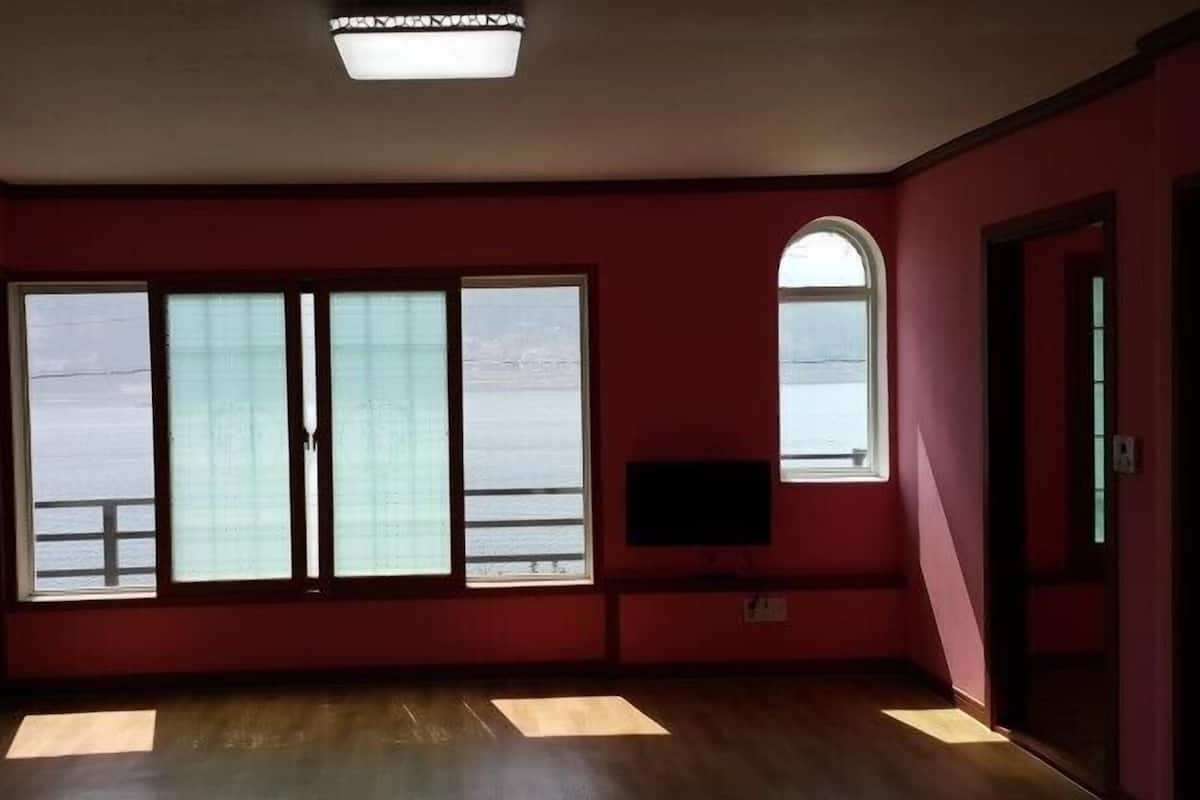 A room with red walls, large windows, a flat-screen TV, and a ceiling light fixture.