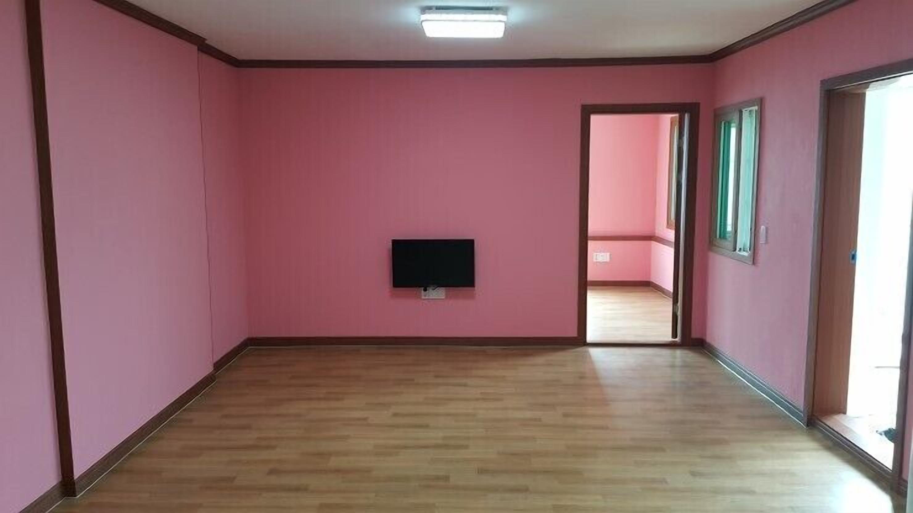 A room with pink walls, a wooden floor, and a television mounted on the wall.