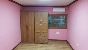 A room with pink walls, a wooden wardrobe with two doors and a small window.