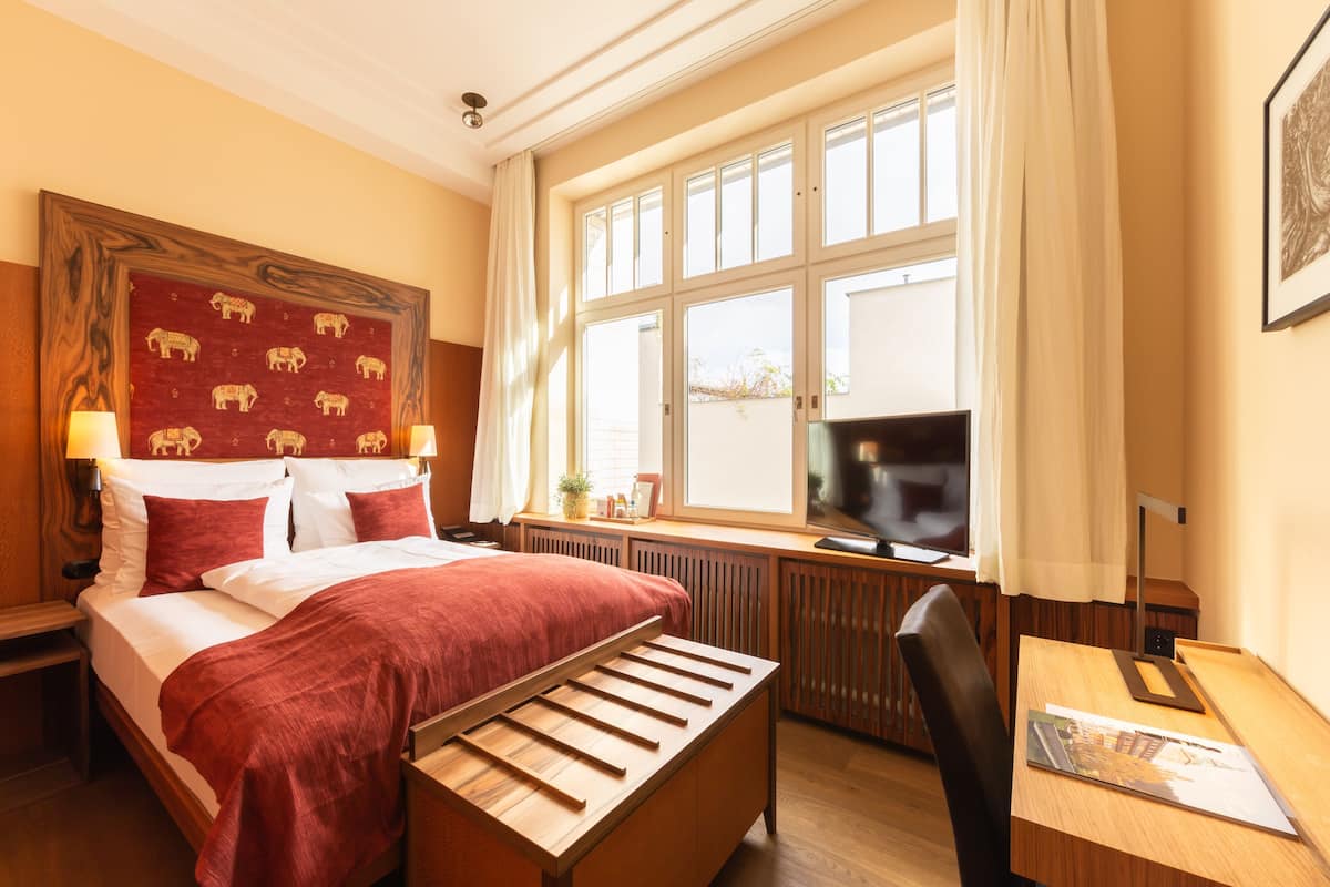 Ein Hotelzimmer mit Bett, Schreibtisch, Stuhl, Fernseher und einem fenster mit Vorhängen.