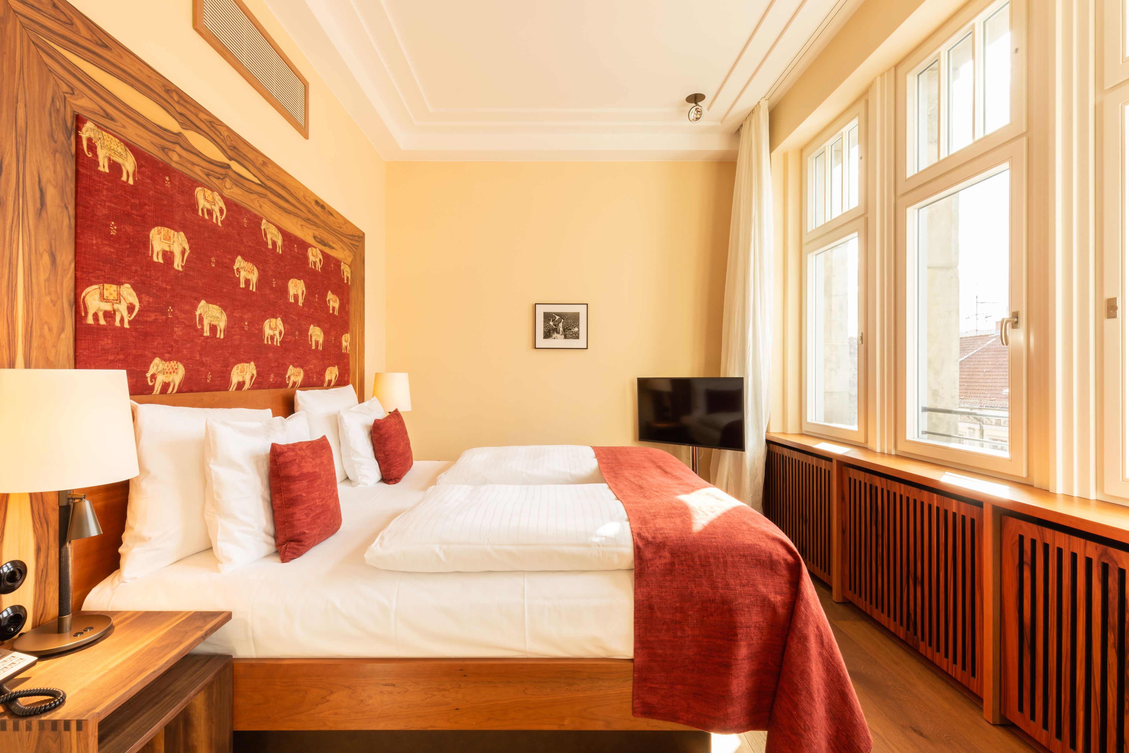 Een hotelkamer met een groot bed, een houten hoofdeinde met olifantmotieven, een televisie en een raam met uitzicht.