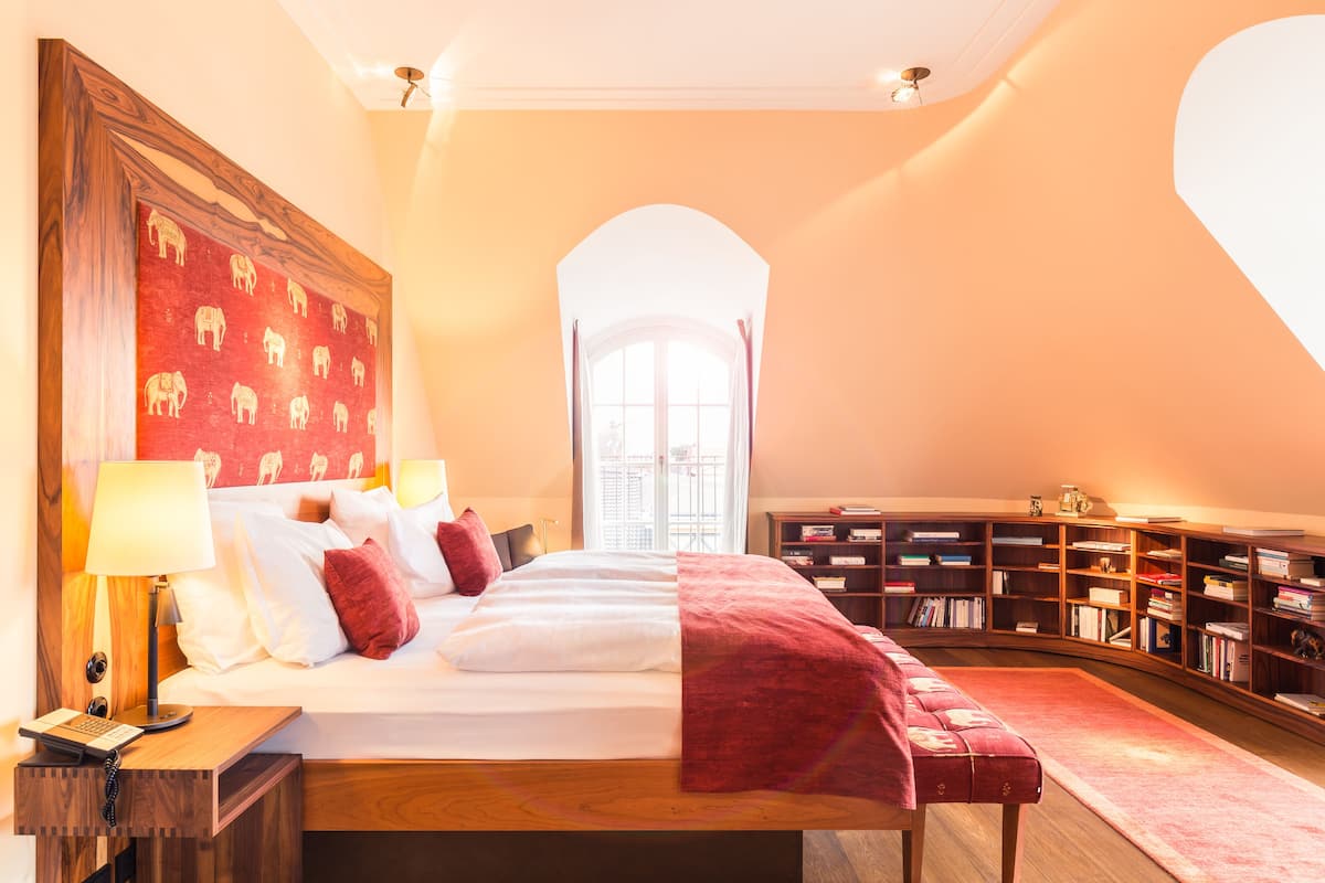 Ein Schlafzimmer mit einem großen Bett, einem hölzernen Kopfteil, einem Nachttisch mit Lampe, einer roten Tagesdecke und einem Bücherregal.