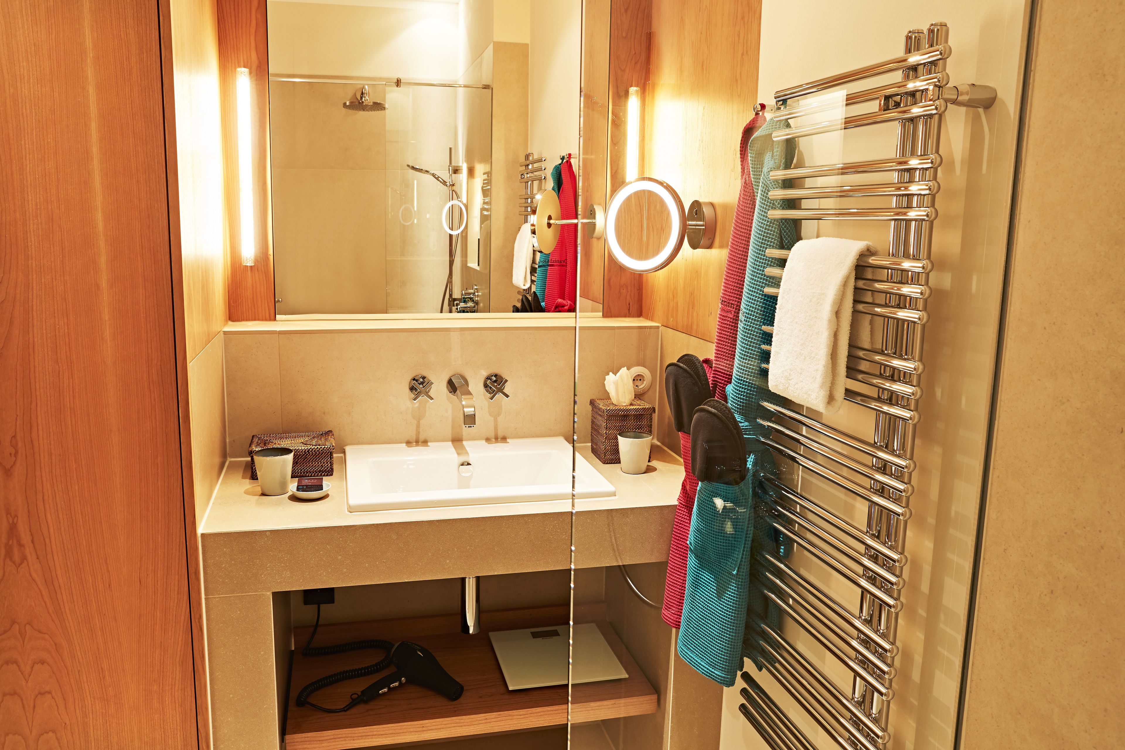 A modern bathroom with a glass-enclosed shower, a white sink, and a towel rack with multiple towels.