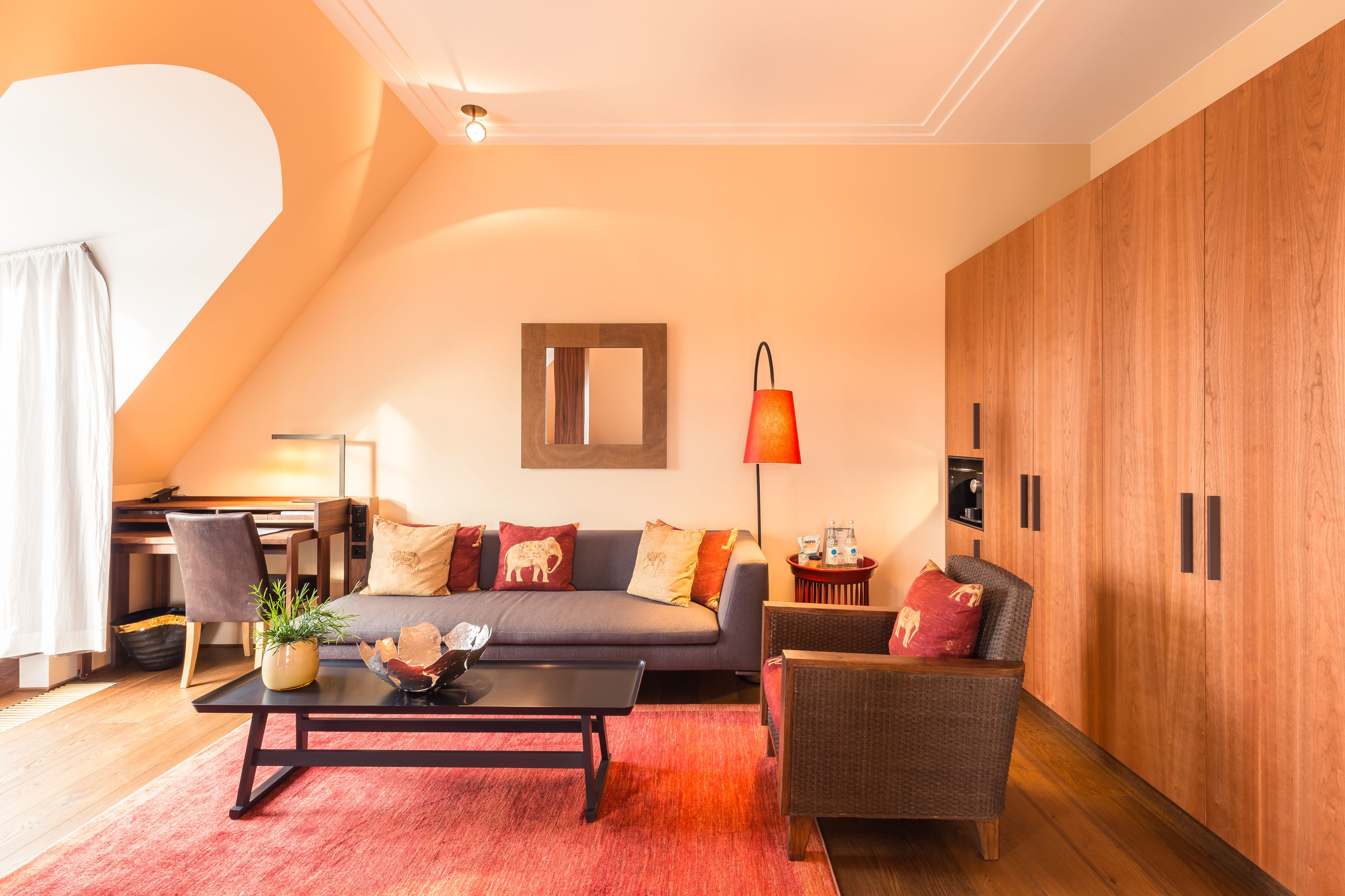 Una sala de estar moderna con un sofá, una mesita de centro y una alfombra roja. Hay un mueble de madera y una lámpara sobre una mesita auxiliar.