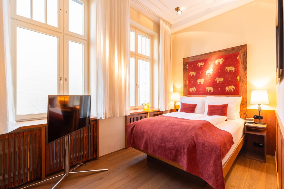 Ein Hotelzimmer mit einem großen Bett, einem Fernseher und einem Fenster mit Vorhängen.