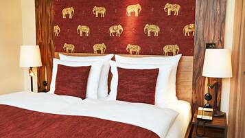 Habitación de hotel con una cama grande, dos lámparas de noche, un cabecero de madera con motivos de elefantes y una mesita de noche con teléfono.