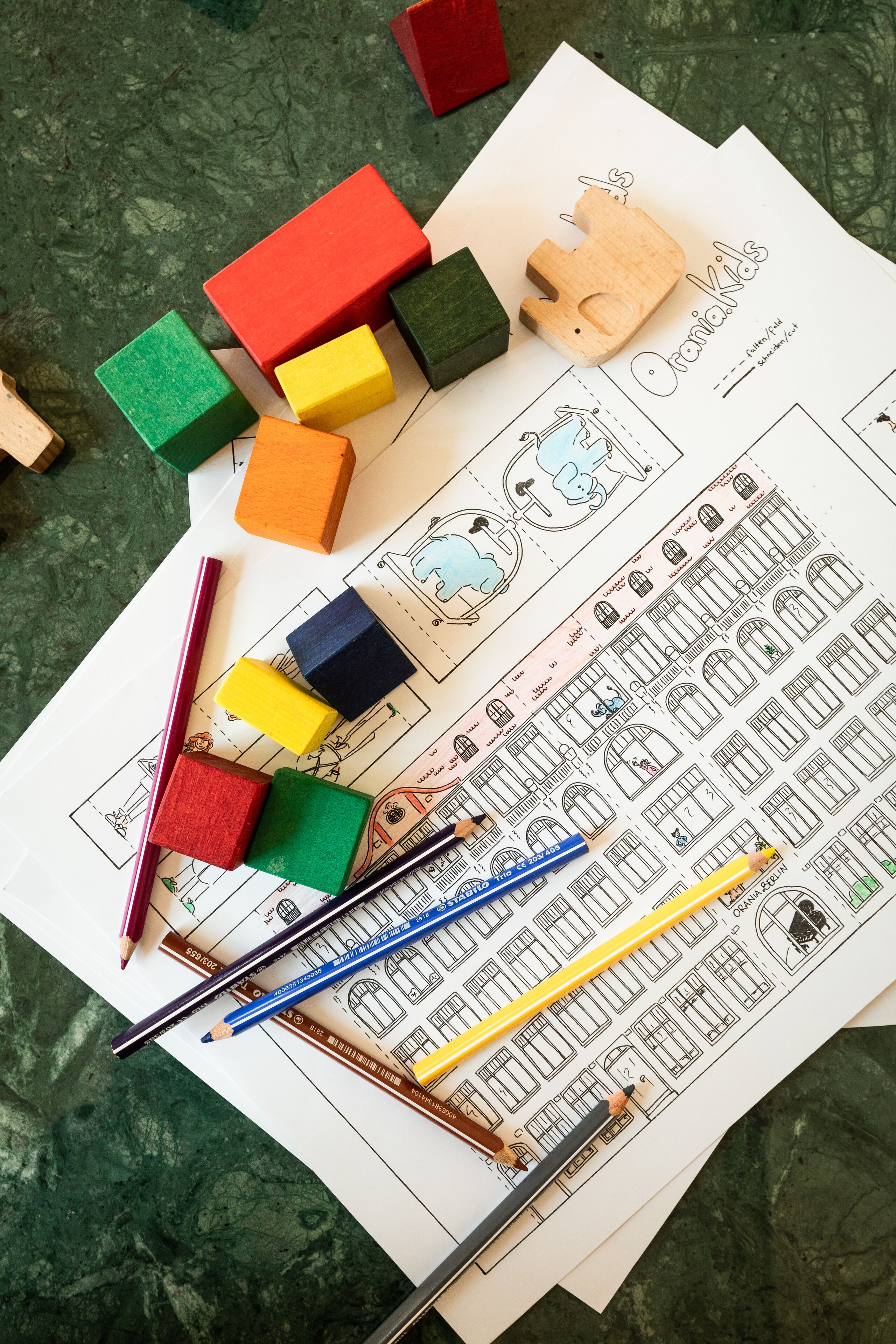 Une vue d’ensemble présentant des blocs de construction colorés, des crayons et une feuille de dessin avec des plans d’architecture.