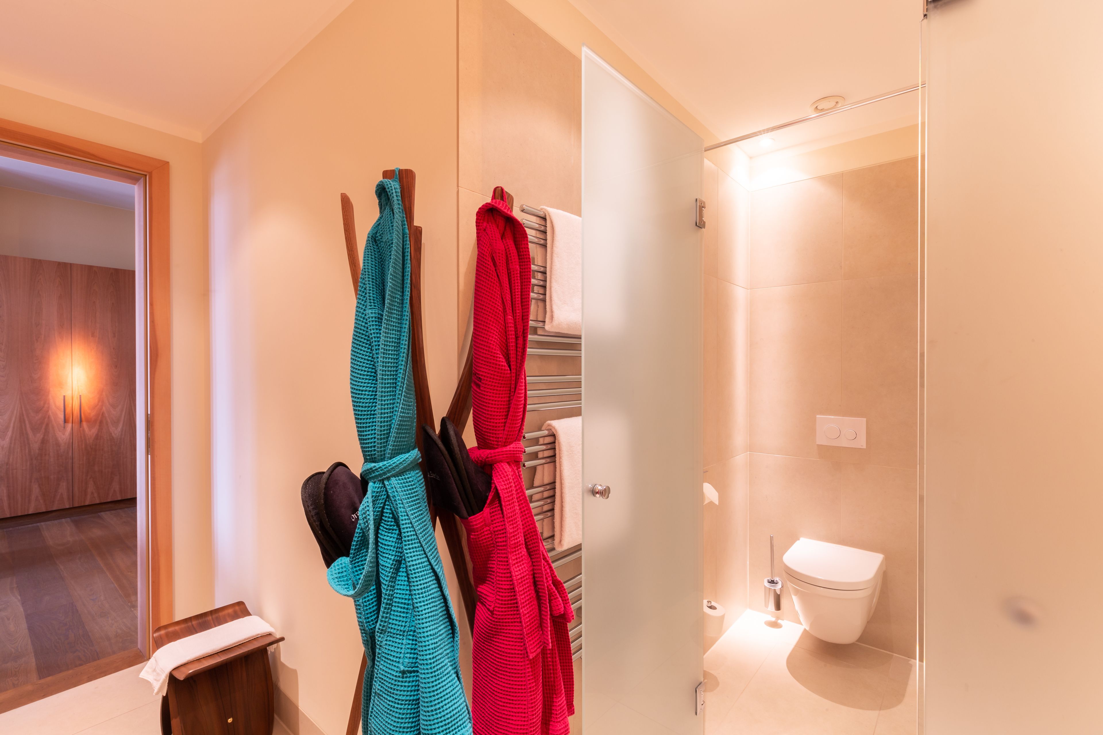 A bathroom with a toilet, a towel rack with towels, and a wooden bench.