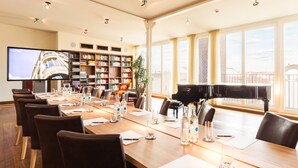 A conference room with a long table, chairs, a piano, a bookshelf, and a TV screen. - Orania.Berlin (Berlin)