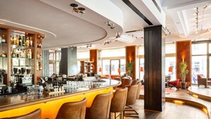 A modern bar area with a curved bar, multiple seating options, and a variety of bottles and glasses on shelves. - Orania.Berlin (Berlin)