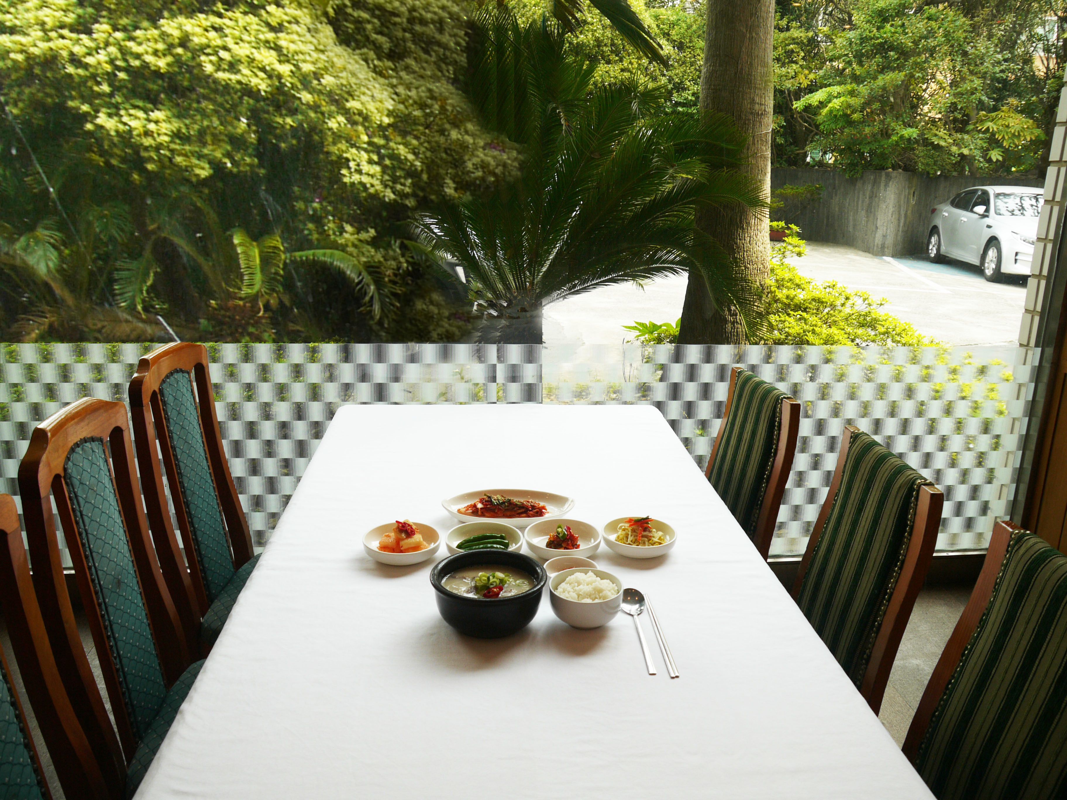 A dining table with a white tablecloth, surrounded by wooden chairs with green upholstery.