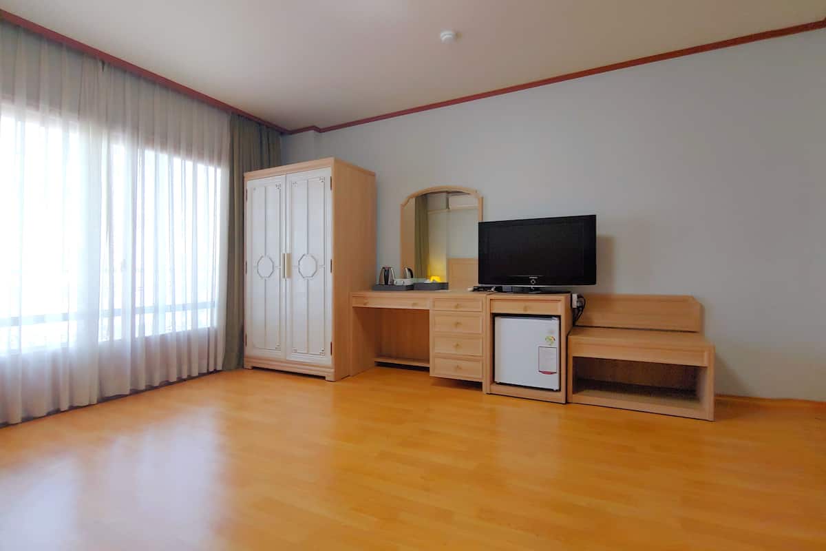Habitación de hotel con escritorio de madera, televisor, armario y refrigerador pequeño.