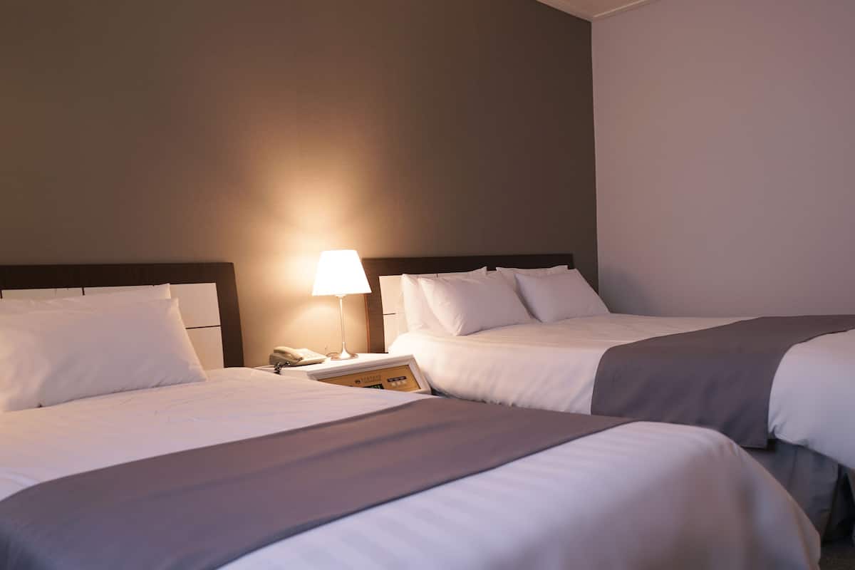 Una habitación de hotel con dos camas, una mesita de noche con lámpara y un teléfono.