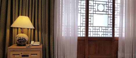 A room with a wooden nightstand, a lamp, a telephone, and a digital clock.
