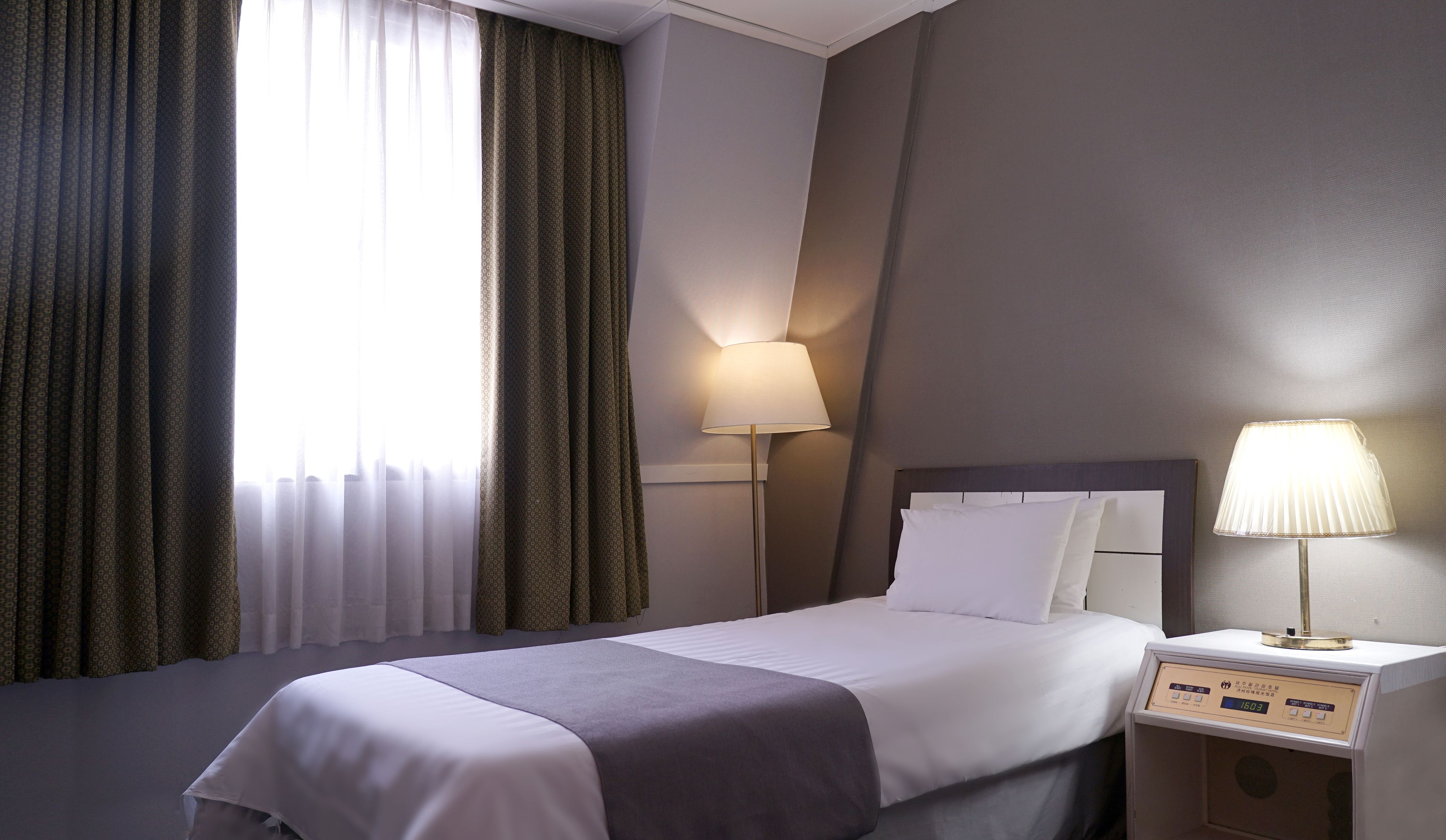 A hotel room with a bed, two bedside lamps, a nightstand, and a window with curtains.