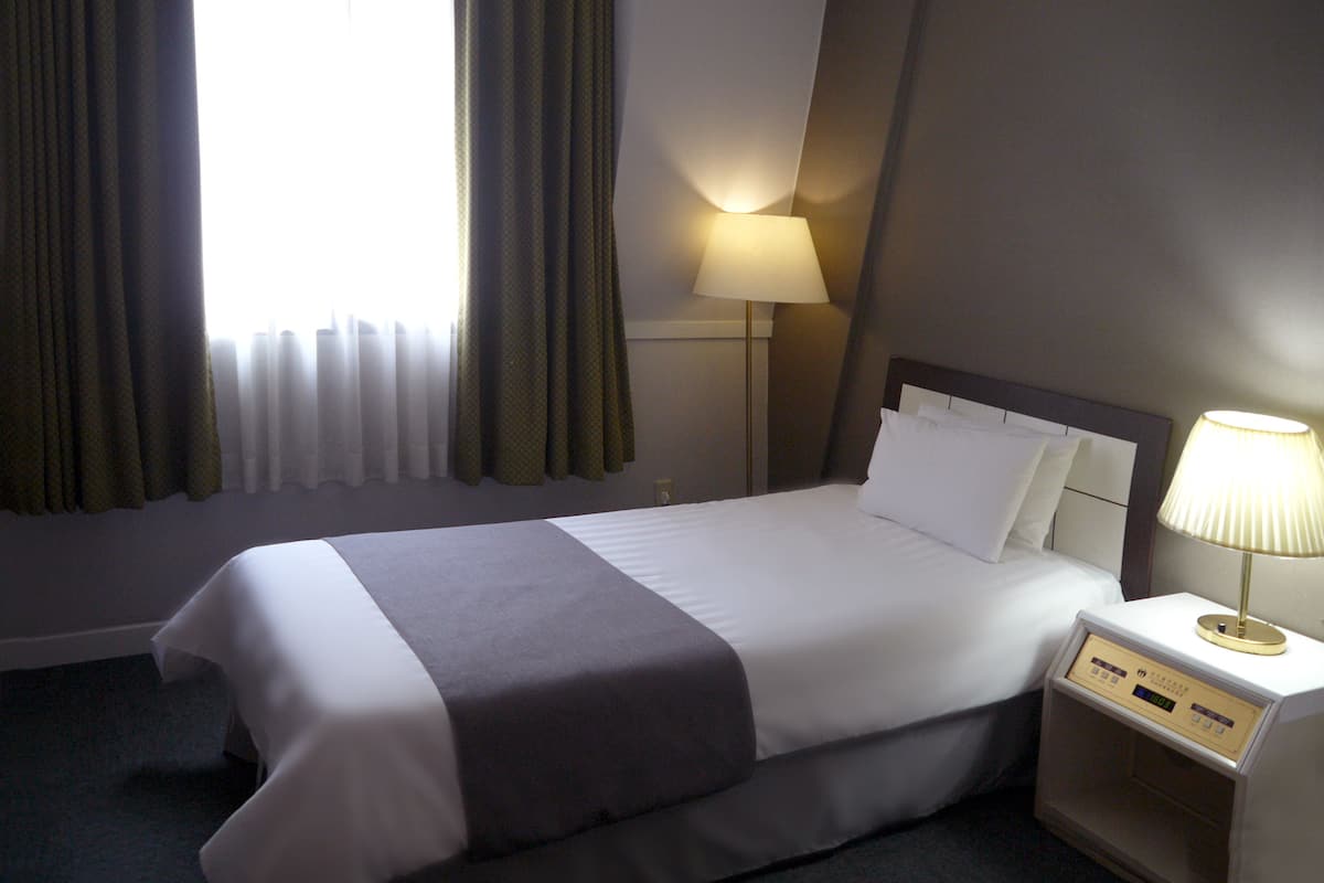 Una habitación de hotel con una cama bien hecha, una lámpara de noche y una ventana con cortinas.