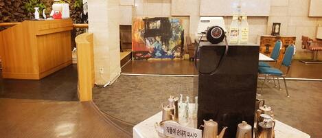 A lobby with a reception desk, a coffee station, and a painting on the wall.