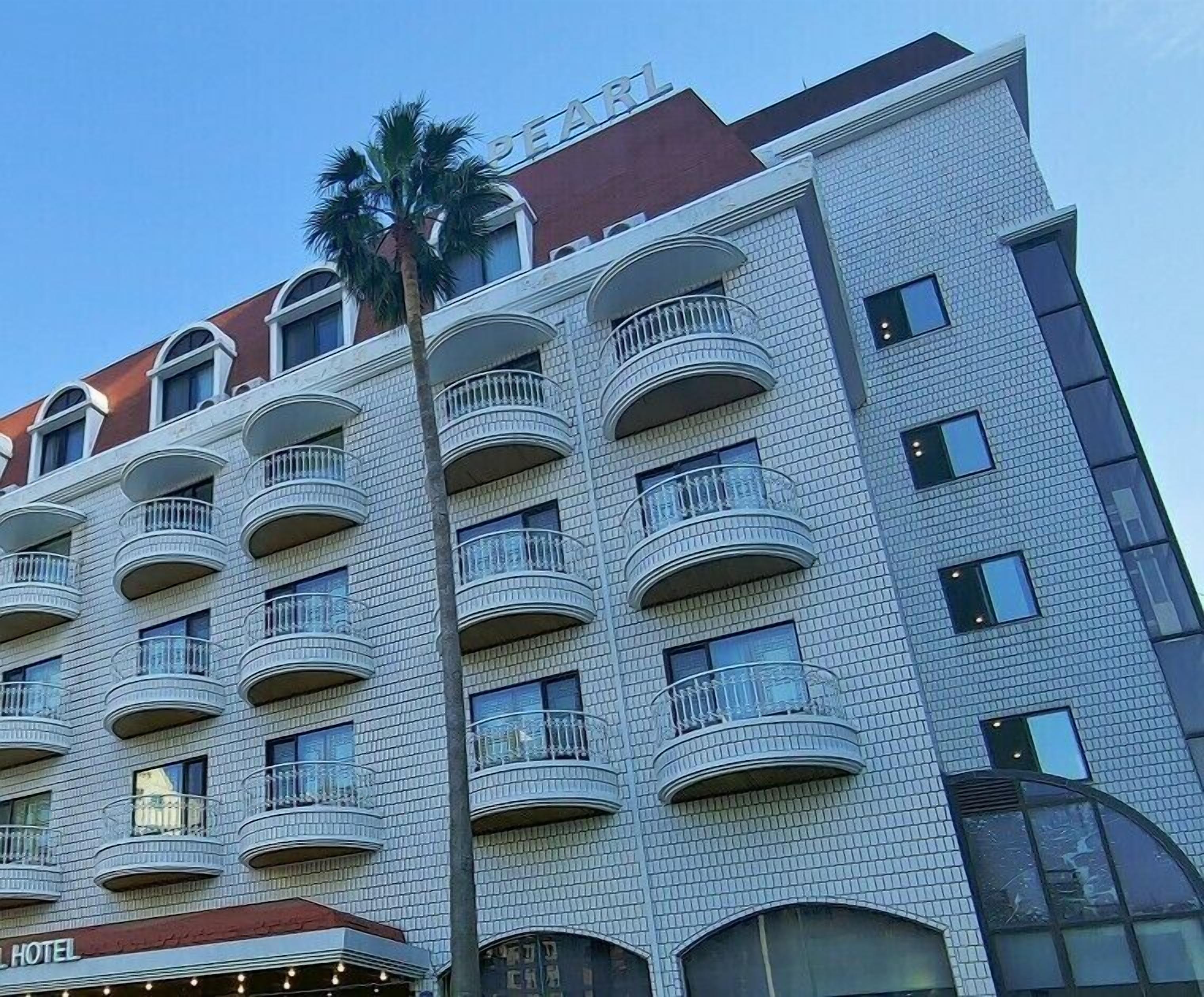 Een meerlaags hotel met balkons op elke verdieping, een rood dak en een herkenbare palmboom.