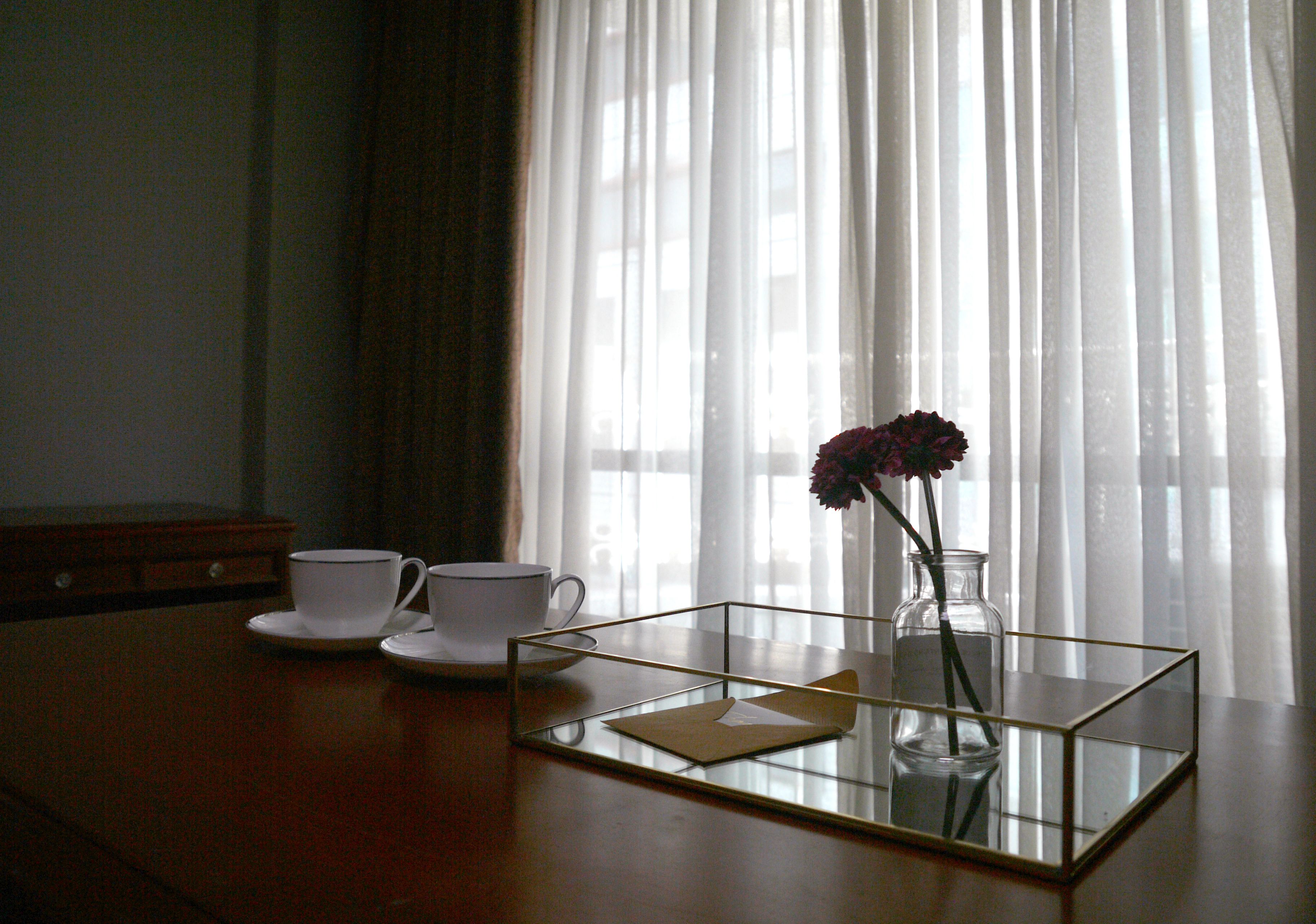 A table with a glass vase containing a flower, two white cups, and a small rectangular tray.