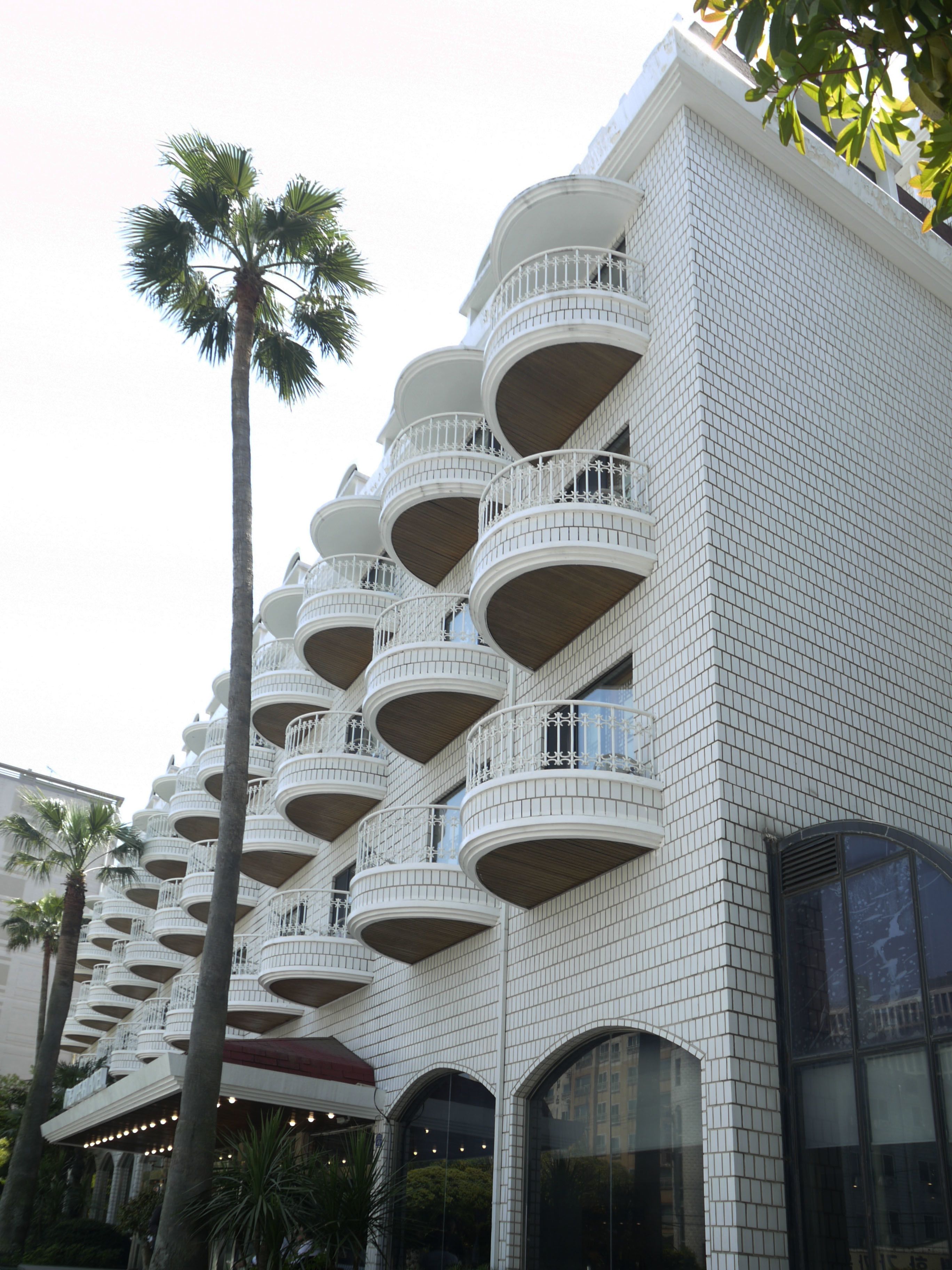 Ein mehrstöckiges Hotel mit Balkonen, Palmen und einer Klinkerfassade.