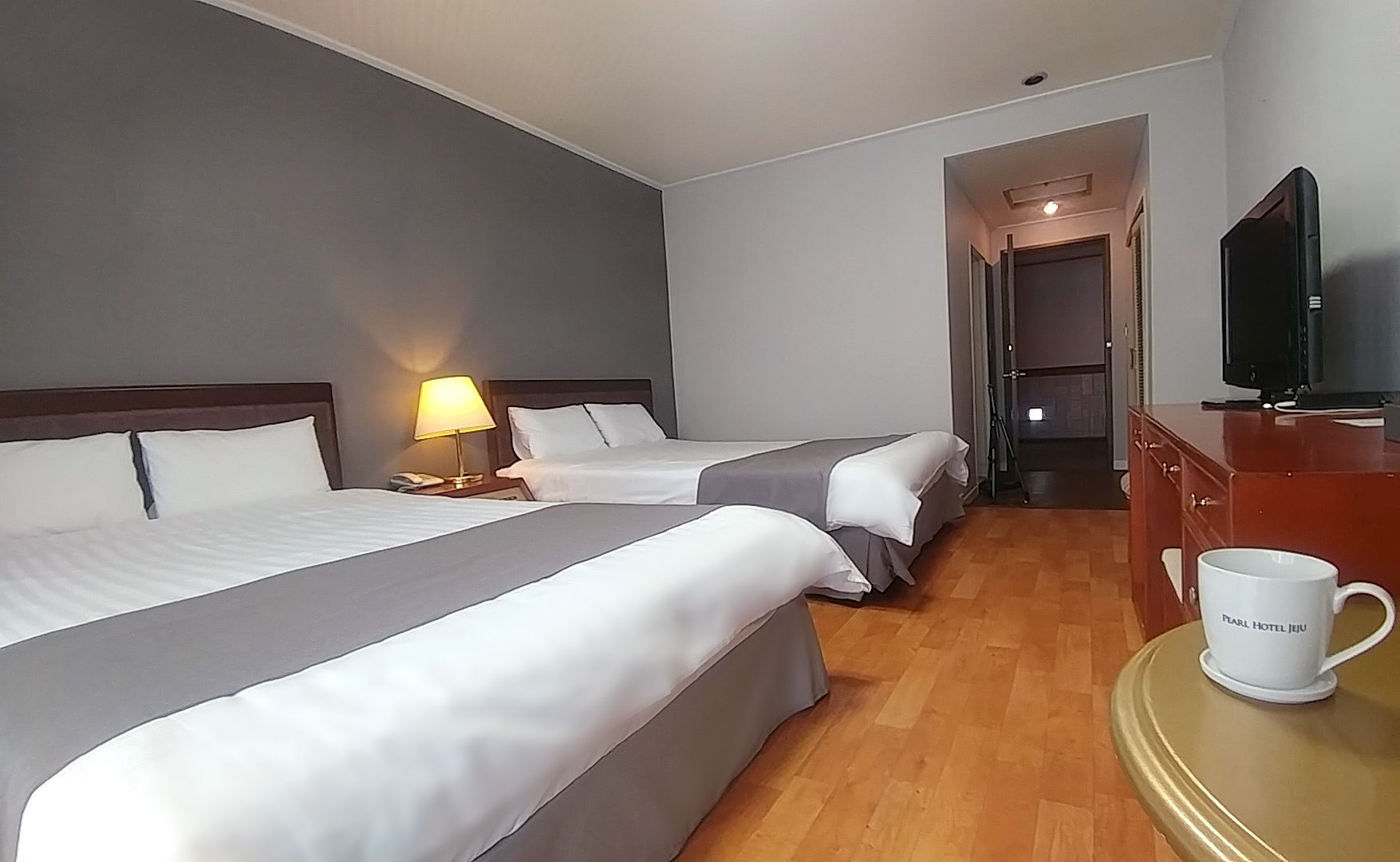 Une chambre d’hôtel avec deux lits, une télévision, une tasse à café et un plancher en bois.