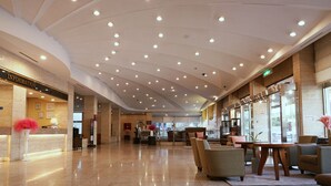 Een ruime lobby met een hoge plafond, een receptiebalie en zithoeken.