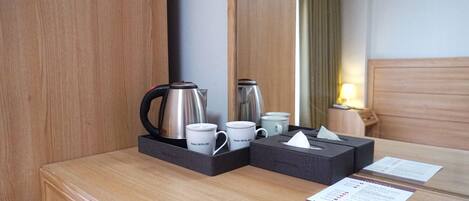 Habitación de hotel con un escritorio de madera, un espejo, una cafetera, dos tazas, una caja de pañuelos y un menú.