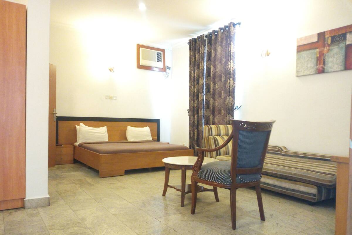 A hotel room with a bed, a chair, a table, and a radiator.