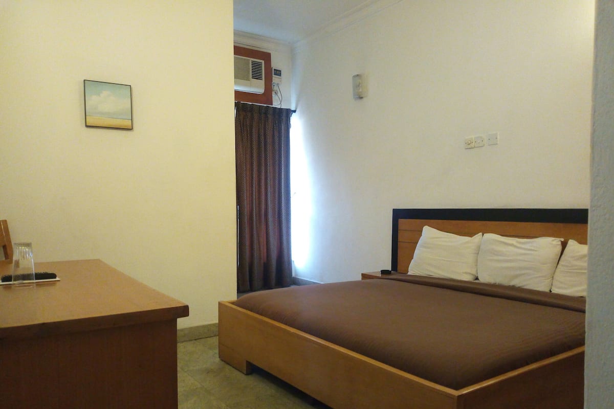 A hotel room with a bed, a desk, and a window with curtains.