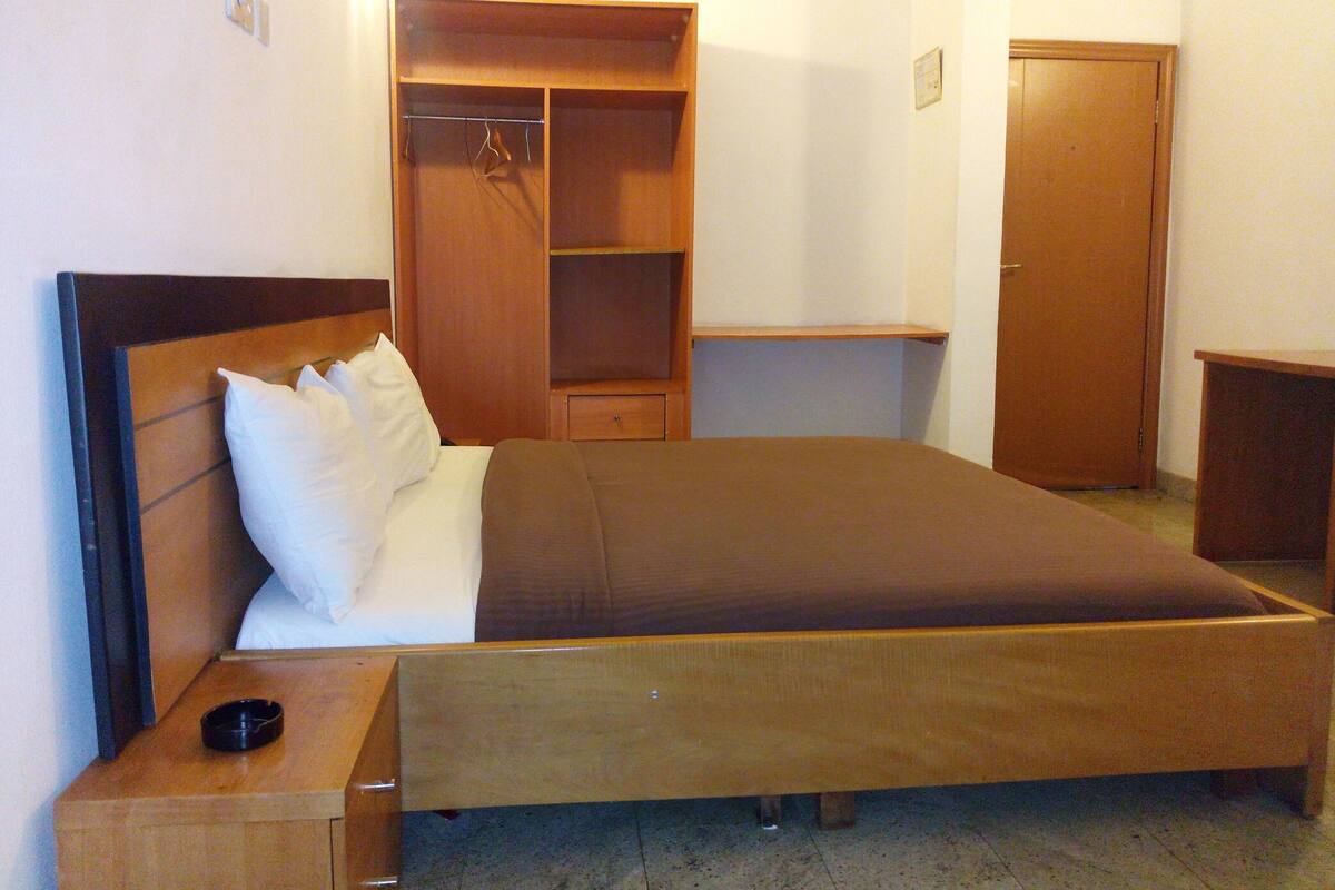 A bedroom with a bed, a wooden wardrobe, a bedside table, and a door.