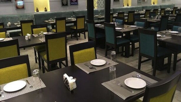 A restaurant with multiple tables and chairs, each set with plates, cutlery, and glasses. - Karma Hotel (Lagos)